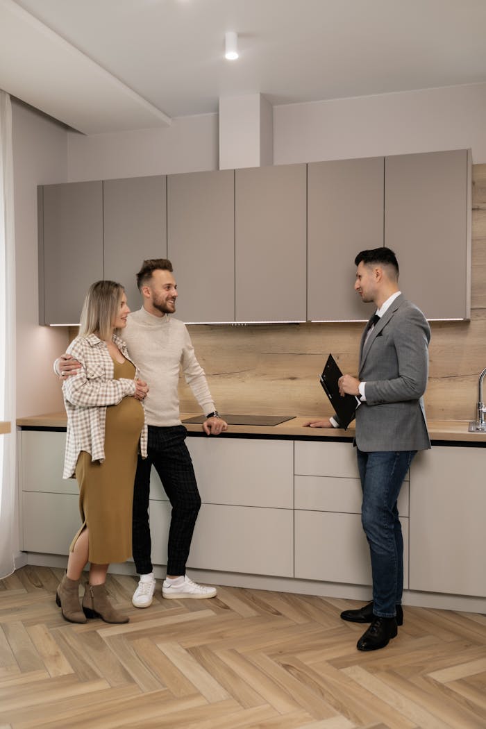 Les retenues locatives : comment éviter les problèmes ? Pregnant couple joyfully discussing their future home purchase with a real estate agent in a modern kitchen.